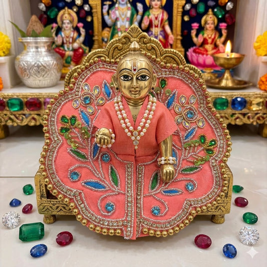 Decorative idol in a pink and gold outfit with gemstones on a white surface.